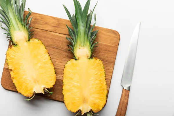 Top view of cut ripe pineapple on wooden chopping board with knife on white background — Stock Photo