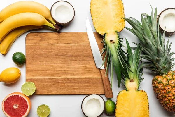 Top view of cut and whole tropical fruits on wooden chopping board with copy space near knife on white background — Stock Photo