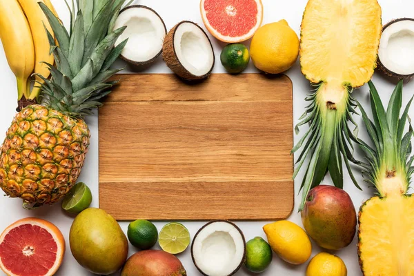 Vista superior de frutas tropicais cortadas e inteiras em torno de tábua de corte de madeira com espaço de cópia no fundo branco — Fotografia de Stock