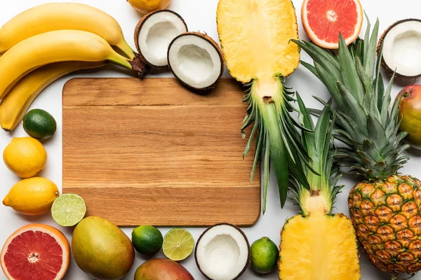 Draufsicht auf geschnittene und ganze exotische Früchte rund um ein hölzernes Schneidebrett mit Kopierraum auf weißem Hintergrund — Stockfoto