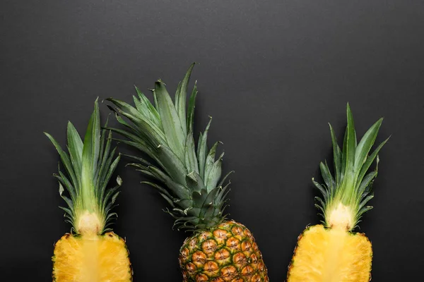 Draufsicht auf reife geschnittene und ganze gelbe Ananas auf schwarzem Hintergrund — Stockfoto