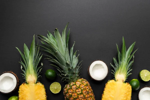 Верхний вид спелых нарезки и целые кокосы, лаймы и ананасы на черном фоне — стоковое фото