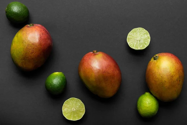 Top view of ripe limes and mango on black background — Stock Photo