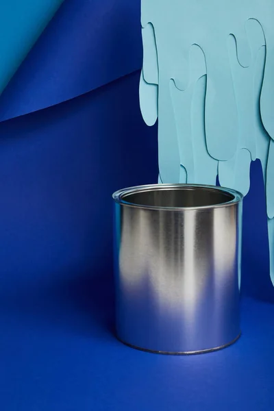 Metal shiny can and dripping paper cut paint on bright blue background — Stock Photo