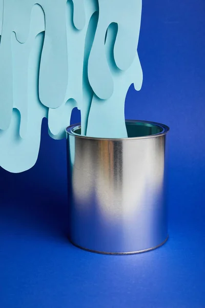 Metal can and dripping paper cut paint on bright blue background — Stock Photo