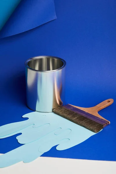 Boîte brillante en métal, pinceau et papier goutte à goutte peinture coupée sur fond bleu vif — Photo de stock