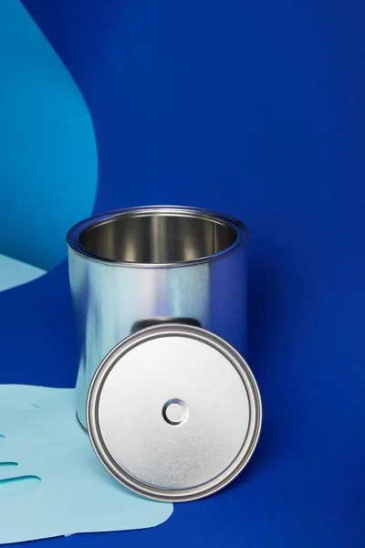 Срібна банка на крапельному папері вирізає фарбу на яскраво-блакитному фоні — стокове фото