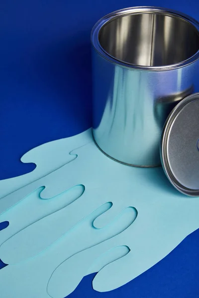 Metal shiny opened can and dripping paper cut paint on bright blue background — Stock Photo