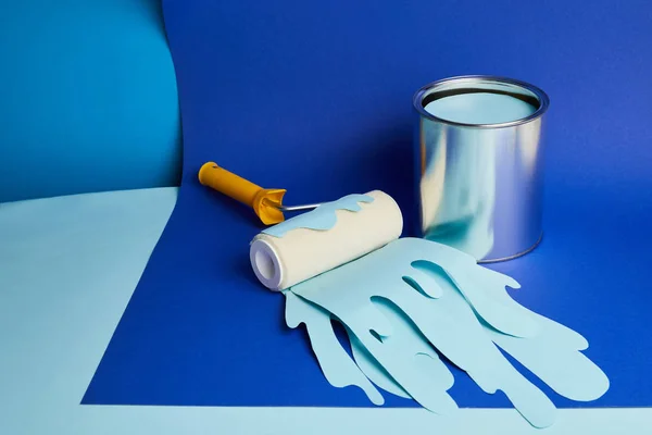 Lata de metal y rodillo con pintura cortada de papel goteante sobre fondo azul brillante - foto de stock