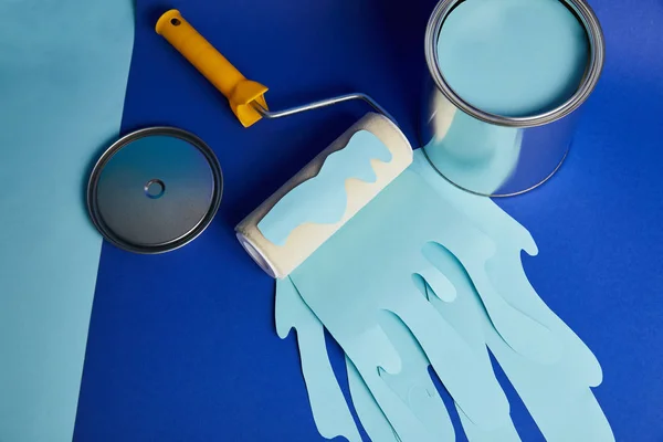 Top view of silver can and roller with dripping paper cut paint on bright blue background — Stock Photo