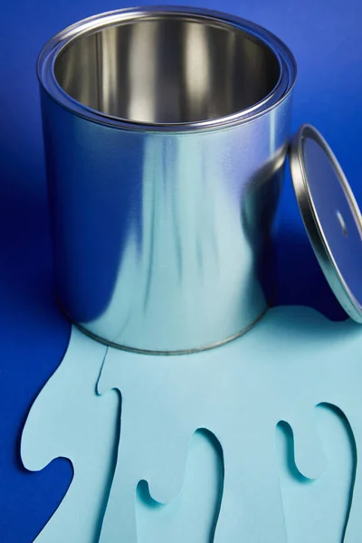 Empty metal shiny can and dripping paper cut paint on bright blue background — Stock Photo