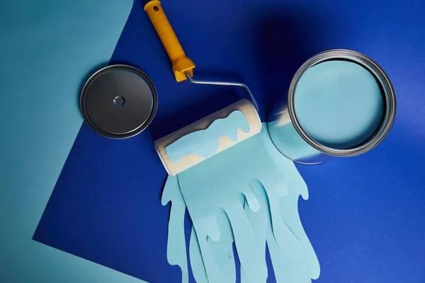 Top view of metal shiny can near roller with dripping paper cut paint on bright blue background — Stock Photo