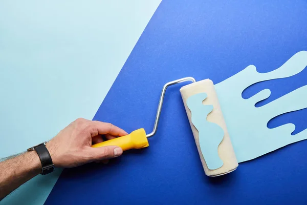 Cropped view of man holding roller with dripping paper cut paint on bright background — Stock Photo