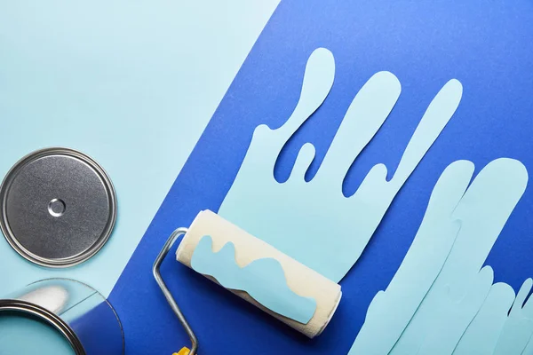 Vue du dessus du capuchon brillant en métal, boîte et papier bleu coupé goutte à goutte peinture près du rouleau — Photo de stock