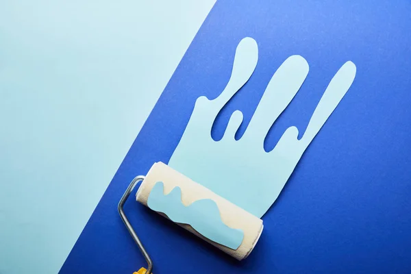 Draufsicht der Walze mit blauem Papierschnitt tropfende Farbe auf hellblauem Hintergrund — Stockfoto