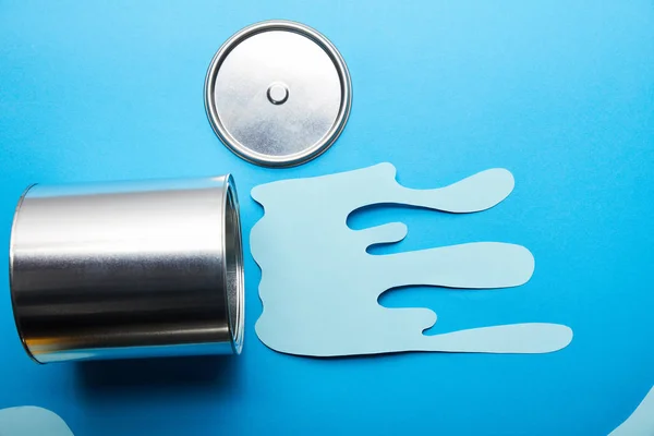 Top view of metal shiny can and can near dripping paper cut paint on bright blue background — Stock Photo