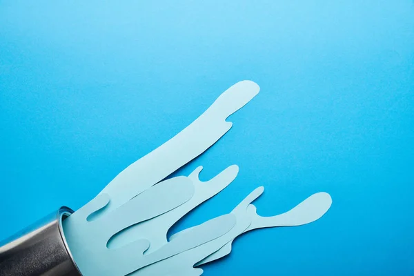 Top view of metal shiny can and spills of paper cut paint on bright blue background — Stock Photo