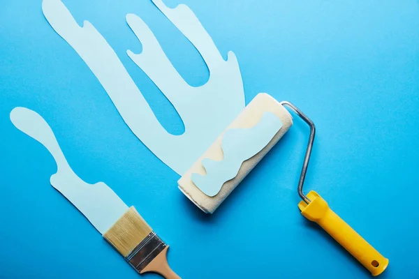 Draufsicht von Rolle und Pinsel mit tropfender Papierschnittfarbe auf hellblauem Hintergrund — Stockfoto