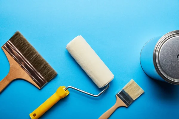 Top view of roller, metal can and brushes on blue background with copy space — Stock Photo