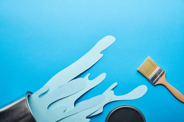 Top view of spilled paper cut blue paint from metal can near brush and cap — Stock Photo