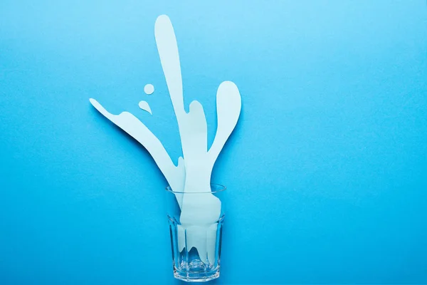 Vue du dessus du verre avec éclaboussure d'eau découpée sur fond bleu — Photo de stock