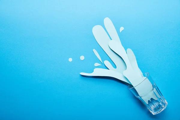 Top view of glass with paper cut water splash on blue background with copy space — Stock Photo