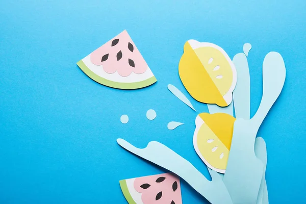 Vue du dessus des éclaboussures d'eau coupées en papier avec des citrons, des feuilles et des pastèques sur fond bleu — Photo de stock