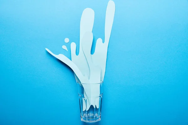 Top view of glass with paper cut water splash on bright blue background with copy space — Stock Photo