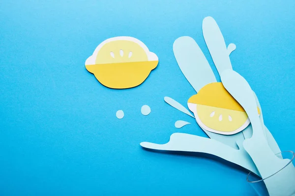 Ansicht von Papier geschnitten Wasserspritzer mit Zitronen in der Nähe von Glas auf blauem Hintergrund — Stockfoto