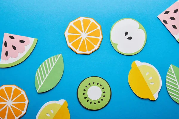 Вид зверху на паперові вирізані лимони, листя, апельсини, ківі та кавуни на синьому фоні — стокове фото