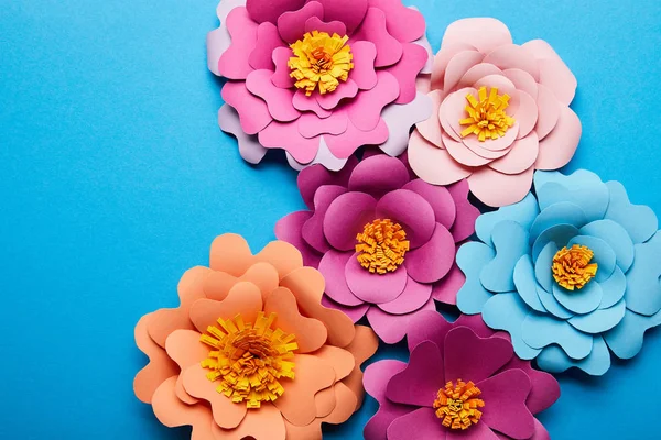 Vue de dessus de fleurs coupées en papier coloré en fleurs sur fond bleu — Photo de stock