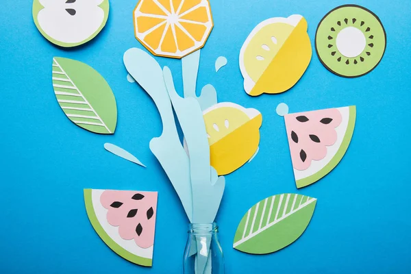 Верхний вид бумаги разрезать брызги воды с фруктами возле стеклянной бутылки на синем фоне — стоковое фото