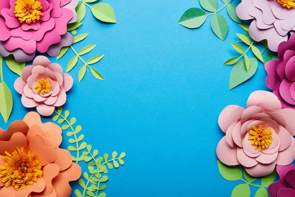 Vista superior de flores de corte de papel multicoloridas com folhas verdes no fundo azul com espaço de cópia — Fotografia de Stock