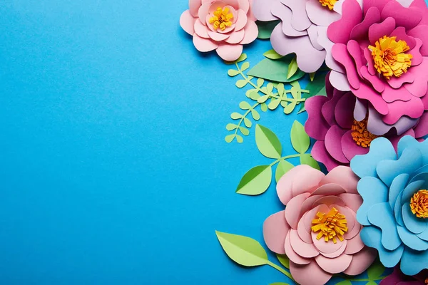 Vue de dessus de fleurs coupées en papier coloré avec des feuilles vertes sur fond bleu avec espace de copie — Photo de stock