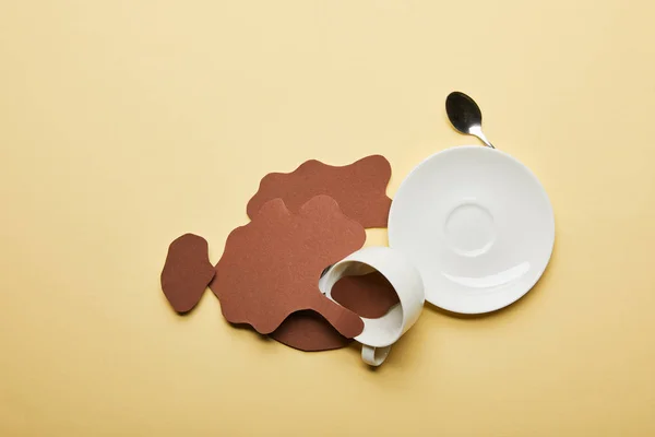 Vista superior de los derrames de café cortados en papel cerca de la taza, platillo y cuchara sobre fondo beige con espacio para copiar - foto de stock