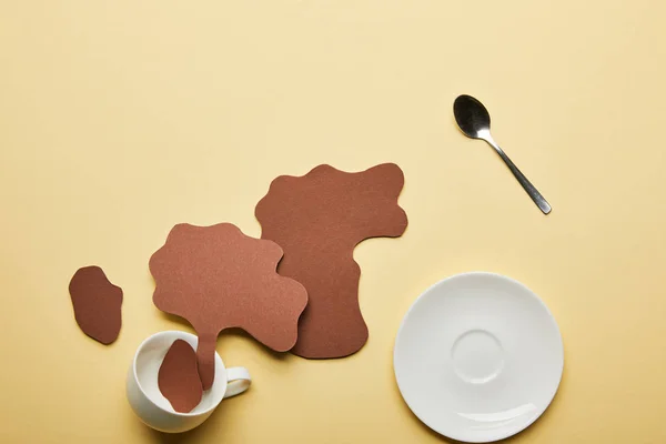 Top view of paper cut coffee spills near white cup, saucer and spoon on beige background — Stock Photo