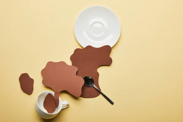 Top view of paper cut coffee spills near cup, saucer and spoon on beige background — Stock Photo