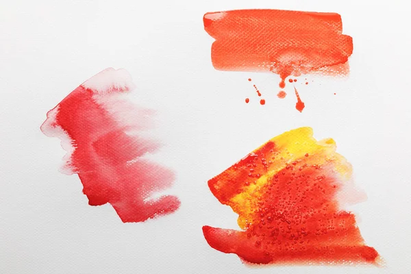 Vue de dessus des coups de pinceau d'aquarelle lumineux mélangés jaunes et rouges sur papier blanc — Photo de stock