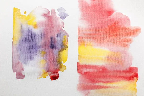 Vue de dessus des coups de pinceau d'aquarelle mixtes jaunes, violets et rouges sur papier blanc — Photo de stock