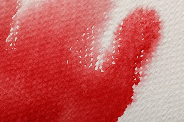Vista de cerca del derrame de pintura de acuarela roja sobre fondo texturizado blanco - foto de stock