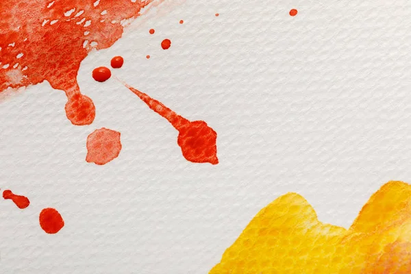 Vue rapprochée des déversements de peinture aquarelle jaune et rouge avec des gouttes sur fond texturé blanc — Photo de stock