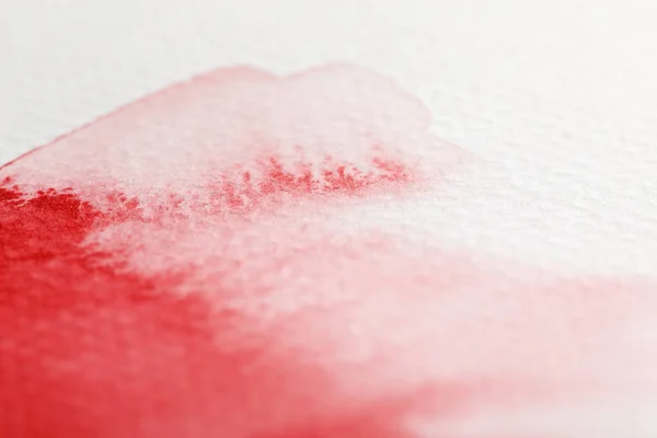 Vista de cerca del derrame de pintura de acuarela roja pálida sobre fondo blanco - foto de stock