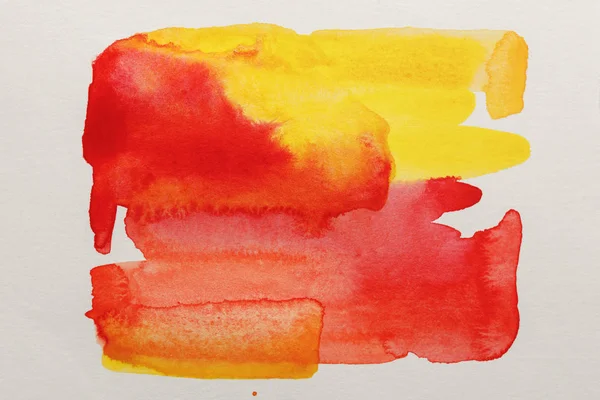 Vista superior de los derrames de pintura de acuarela amarilla y roja sobre papel blanco - foto de stock