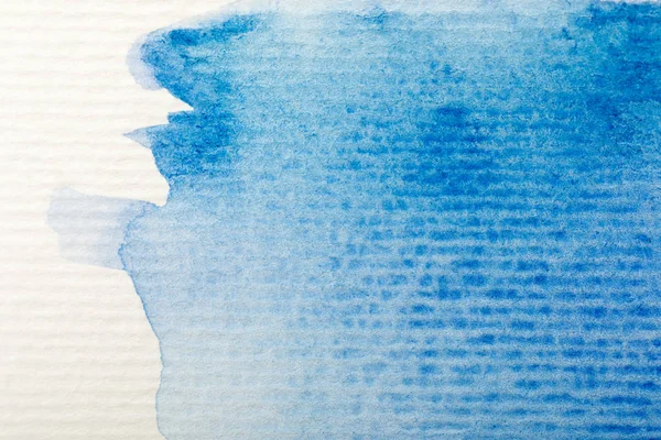 Vue rapprochée du déversement de peinture aquarelle bleue sur fond de papier texturé blanc — Photo de stock