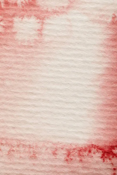 Vista de cerca del derrame de pintura de acuarela brillante roja sobre fondo de papel texturizado - foto de stock