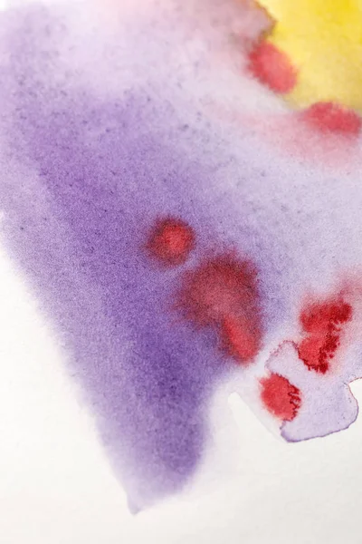 Close up view of yellow, purple and red watercolor paint spills on white paper — Stock Photo