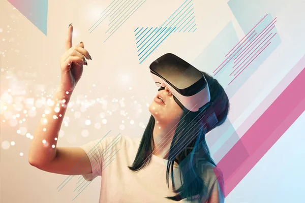 Young woman in virtual reality headset pointing with finger at glowing abstract illustration on beige background — Stock Photo