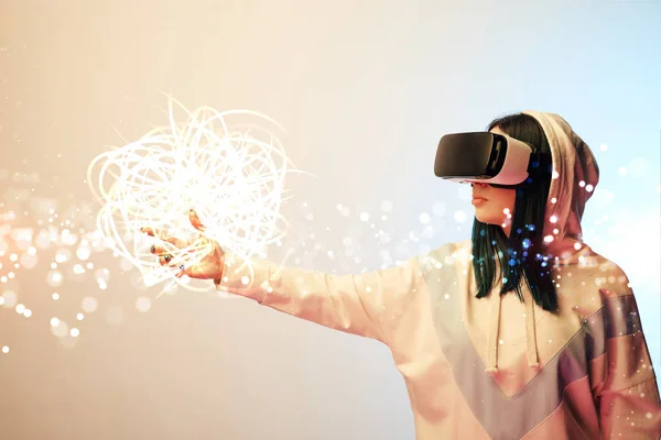 Mujer joven con auriculares de realidad virtual apuntando con la mano a la brillante ilustración cibernética sobre fondo beige y azul - foto de stock