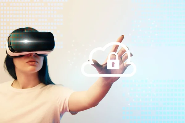 Young woman in virtual reality headset pointing with hand at internet security illustration on beige and blue background — Stock Photo