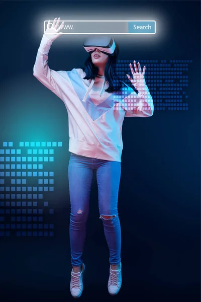 Young excited woman in virtual reality headset levitating in air among glowing data illustration on dark background with search bar above head — Stock Photo